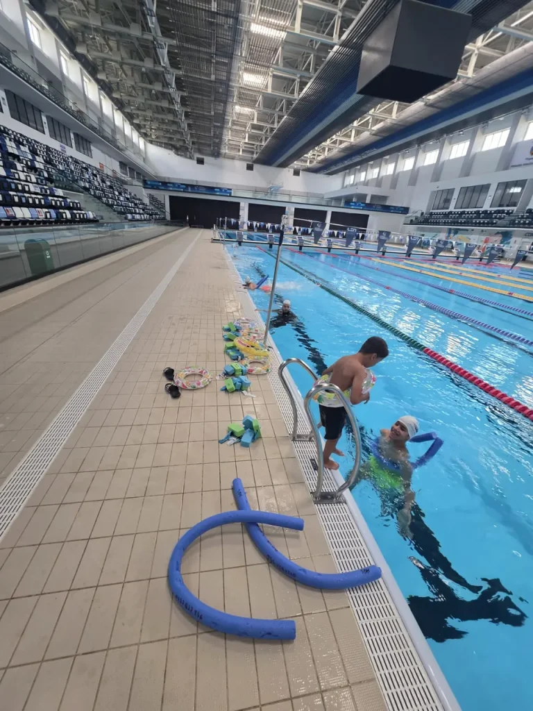 Instructor care asistă un copil la scara de acces în bazin