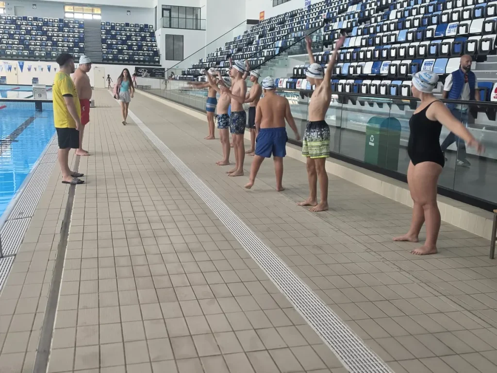 Antrenori și copii pregătind exercițiile pe marginea bazinului Otopeni